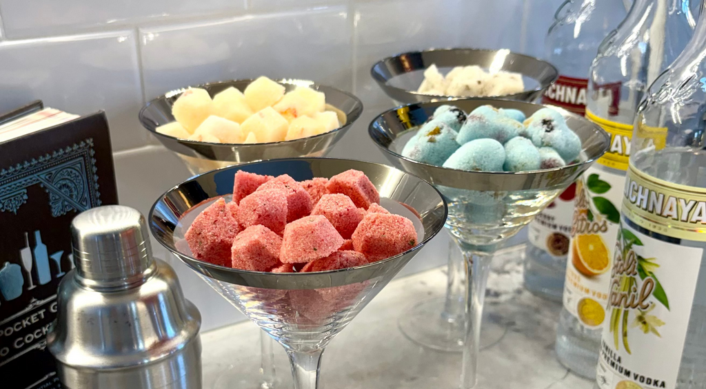 martini glasses full of sugar gems, cocktail shaker, and bottles on a marble surface